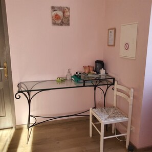 Una habitación pequeña con una mesa de vidrio, una silla blanca, un cuadro en la pared y una puerta con cerradura.