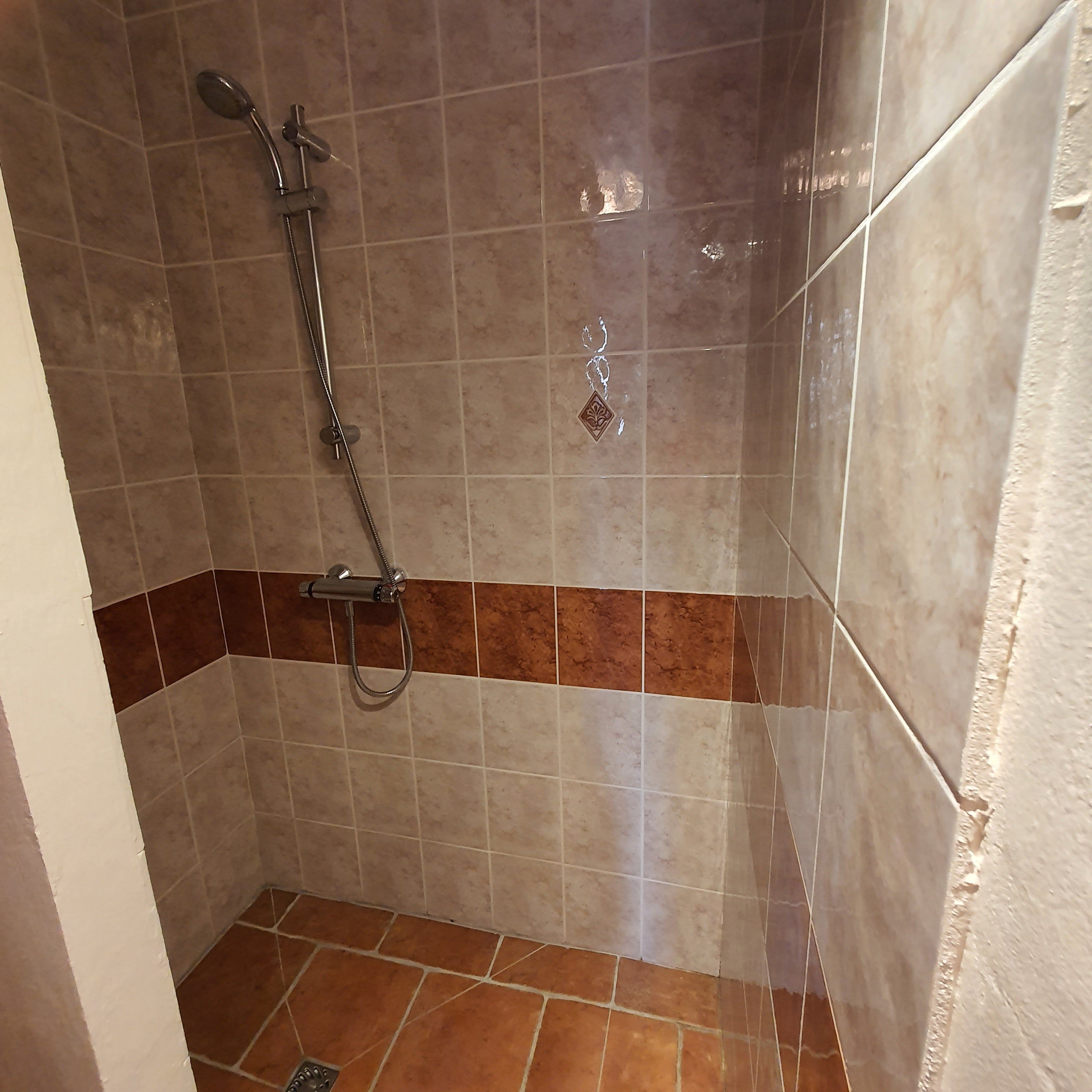 Un área de ducha con un cabezal de ducha de mano y una llave de pared.