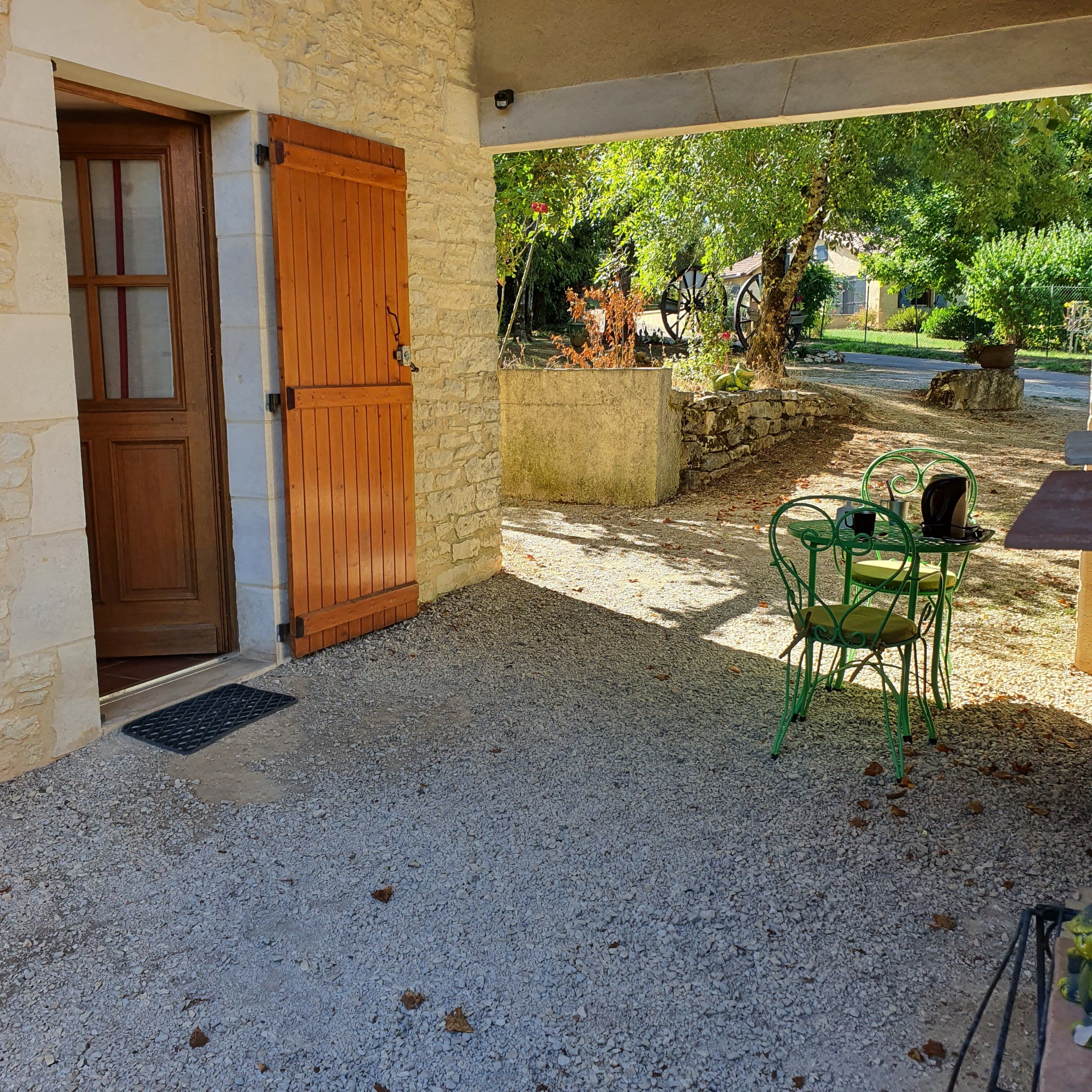 Un espacio al aire libre con techo, pared de piedra, puerta de madera y suelo de grava.