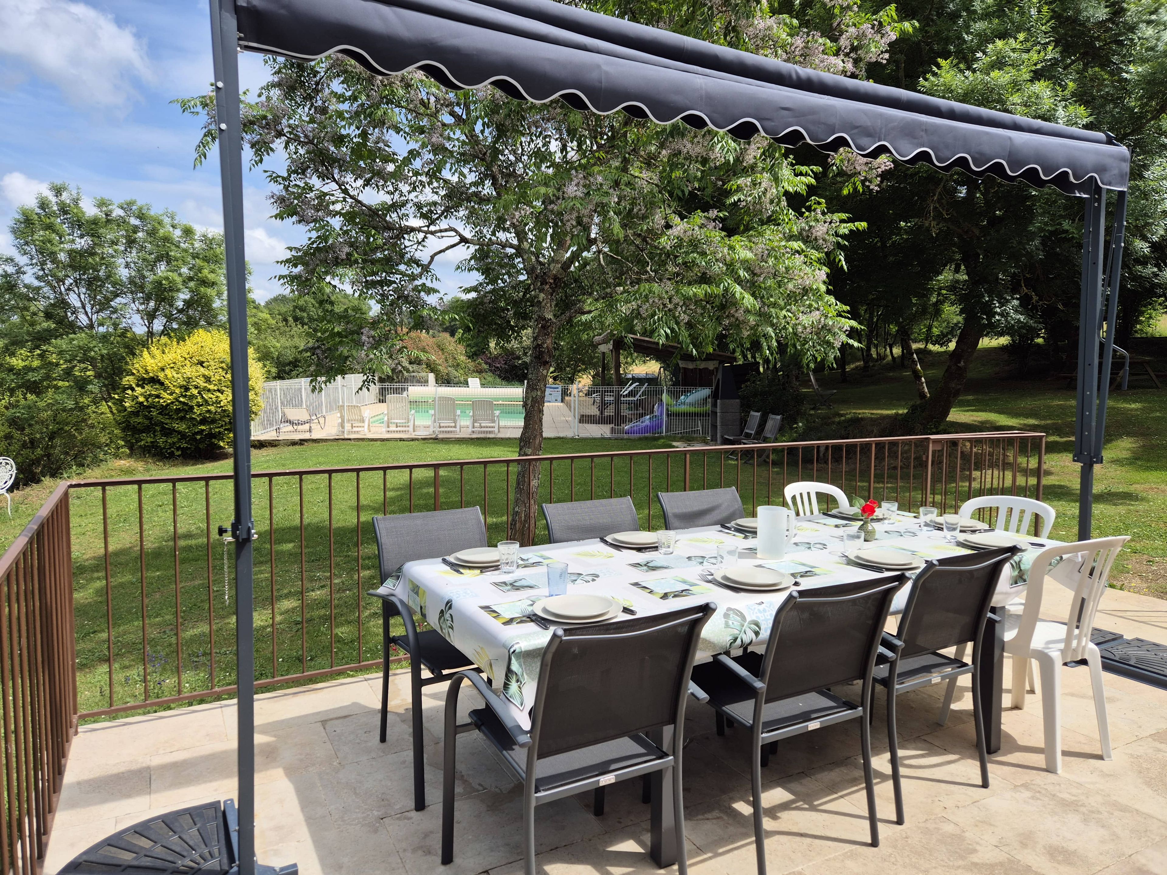 Un patio exterior con una mesa lista para comer, rodeado de sillas y una zona cubierta con barandilla.
