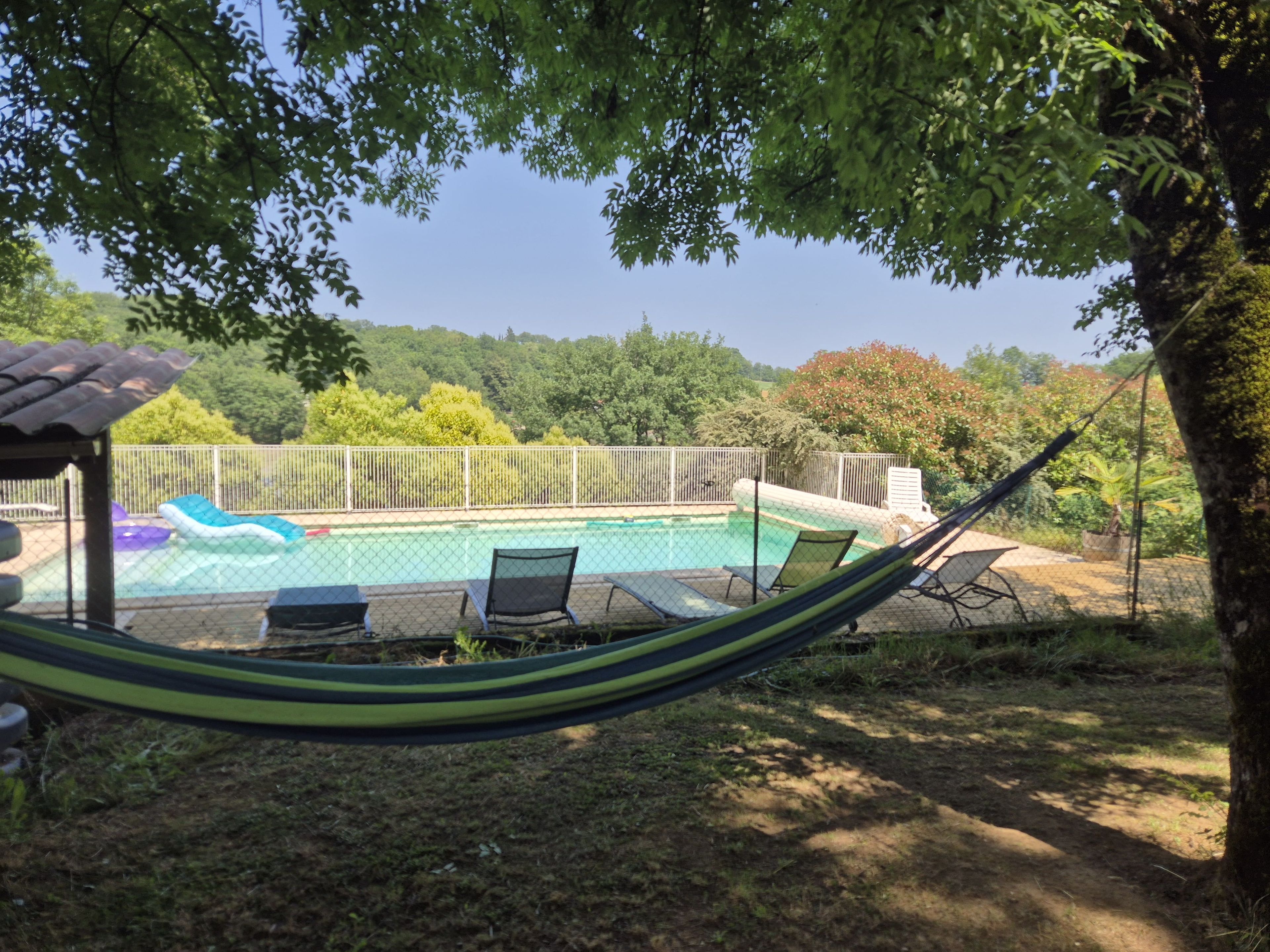 A pool area with a hammock, lounge chairs, and a fenced swimming pool.