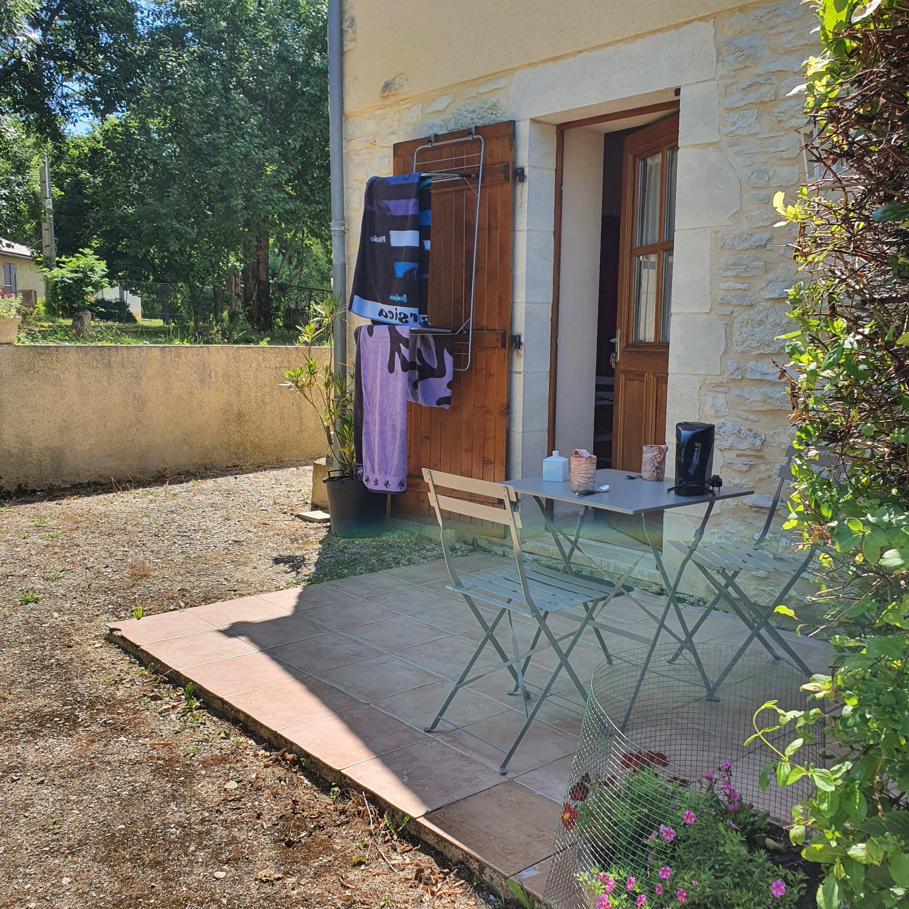 A patio with a table and chairs, a hanging laundry rack, and a small garden area with flowers.