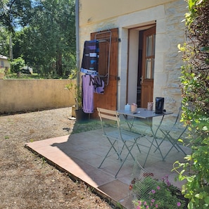 Un patio con una mesa y sillas, un tendedero y un pequeño jardín con flores.