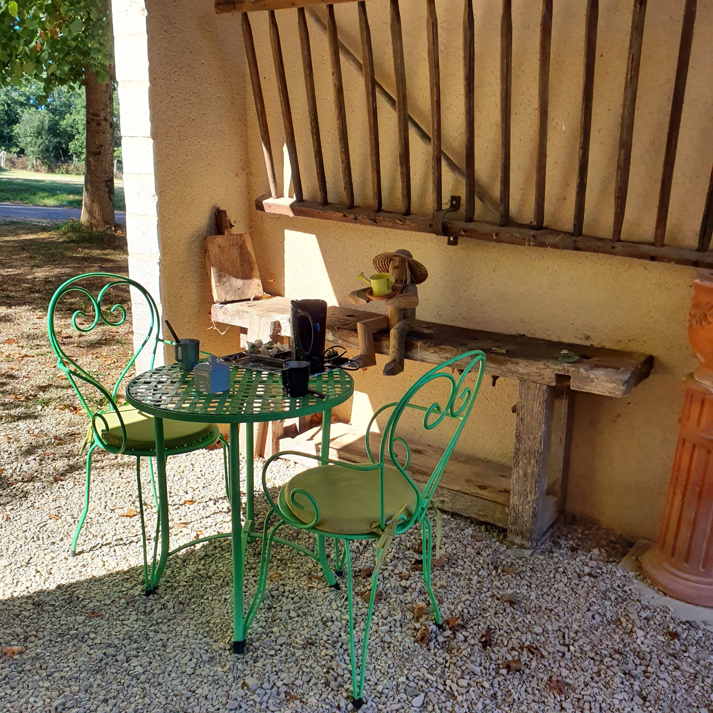 A patio with a metal table and chairs, a wooden bench, and a rustic wall.