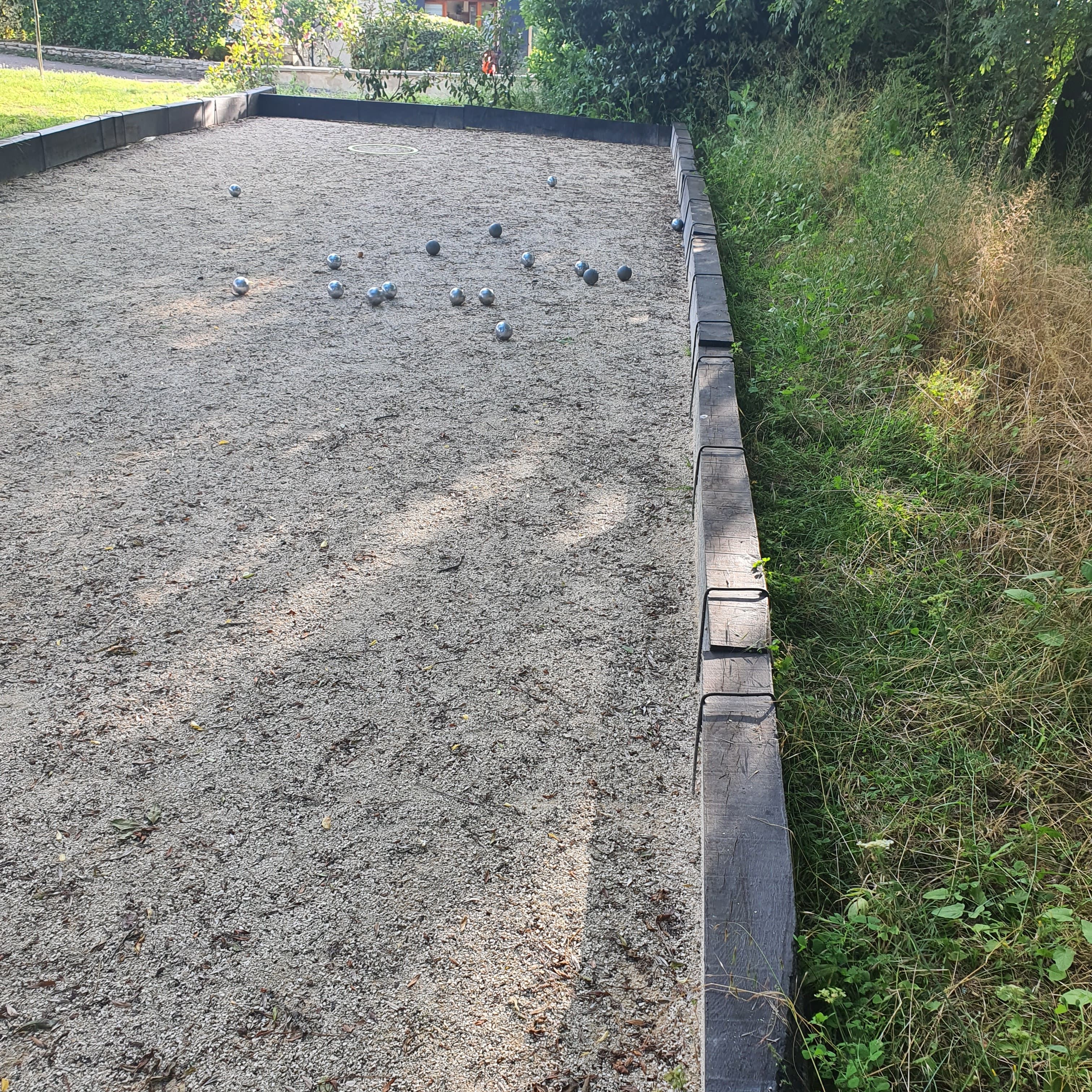 Una cancha de grava con borde de madera y varias pelotas de metal dispersas.