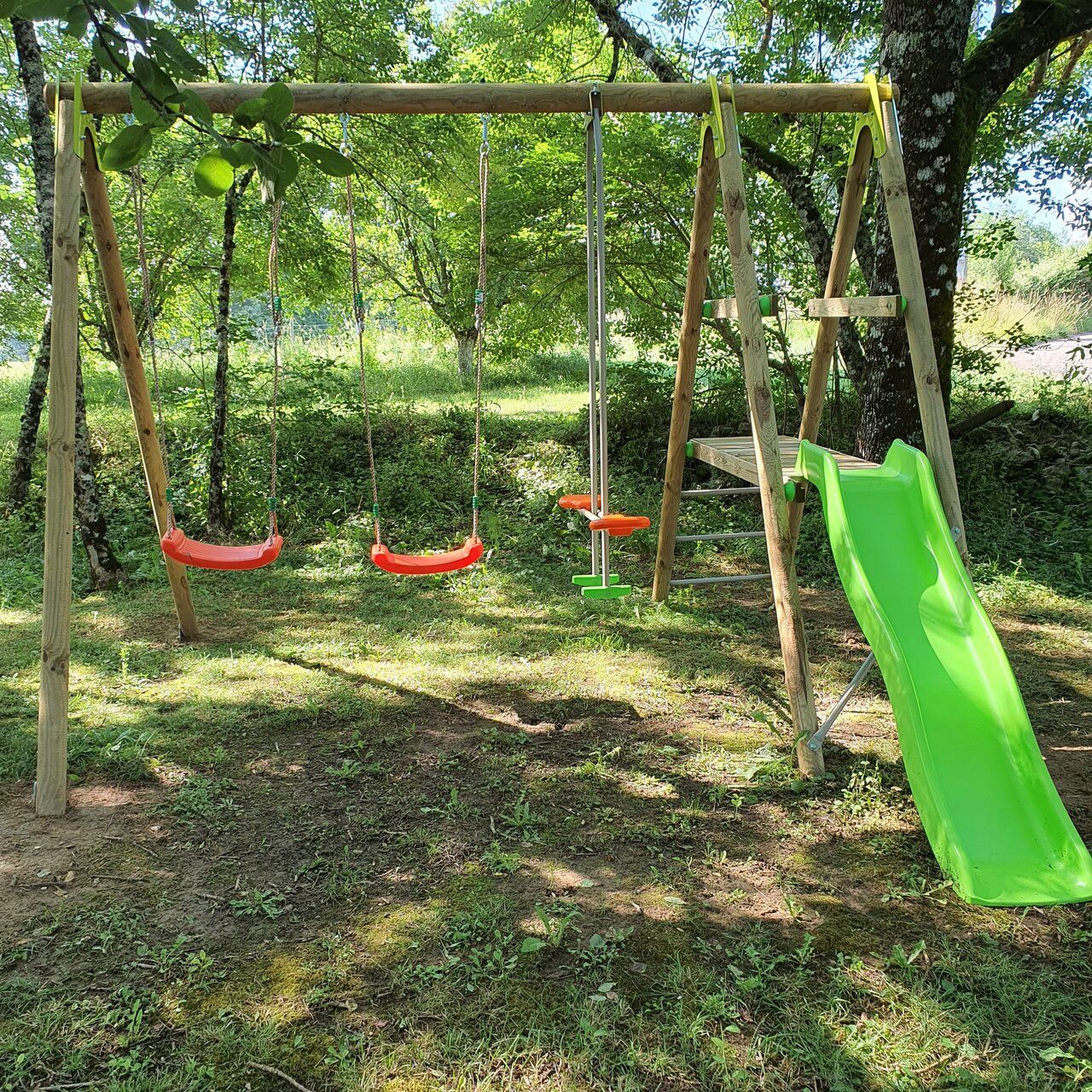 A wooden swing set with two swings and a green slide in a wooded area.