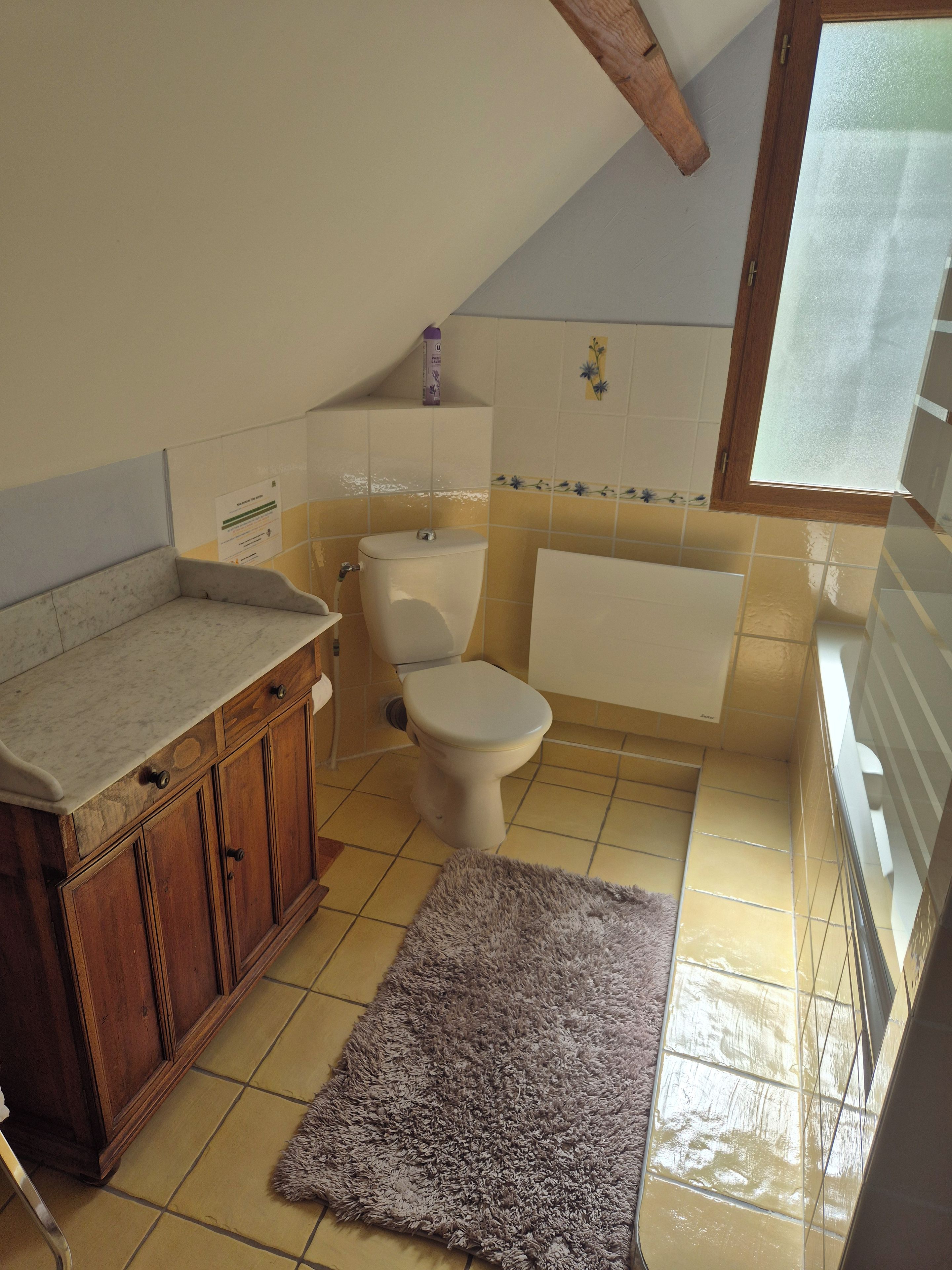 Un baño con inodoro, bañera, armarios de madera y piso de baldosas.