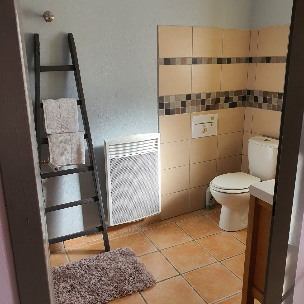 A bathroom with a white toilet, a towel rack with white towels, a radiator, and a tiled shower area.