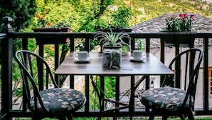 Een balkon met een tafel, twee stoelen, een bloempot en een theepot.