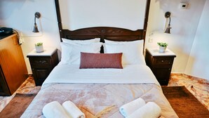 Una cama bien hecha con sábanas blancas, un cabecero de madera y dos mesitas de noche con lámparas.