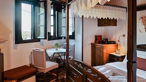 Een slaapkamer met een hemelbed, een bureau met stoel, een nachtkastje met lamp en uitzicht door het raam.