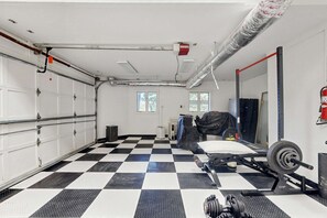 A garage with a checkered floor, a weightlifting station, and a garage door. - Glass Contemporary House, Panoramic Views, 4 Fireplaces, Game Room, Gym, Dog-Friendly (Highlands)
