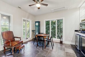 A spacious dining area with a wooden table and chairs, a vintage clock, and large windows offering a view of trees. - Glass Contemporary House, Panoramic Views, 4 Fireplaces, Game Room, Gym, Dog-Friendly (Highlands)