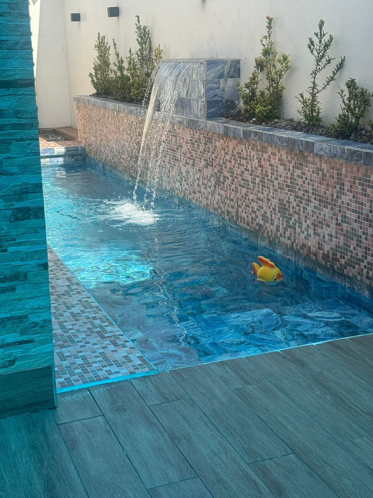 Une piscine avec une cascade et un jouet gonflable jaune.