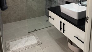 A modern bathroom with a glass-enclosed shower, a white sink, and a black countertop. - Welcome to Villa Sol y Mar, an ideal place for families and couples. (La romana)
