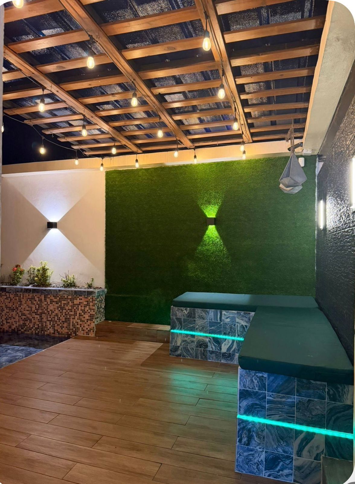 An outdoor patio with a wooden ceiling, green artificial grass wall, and a tiled bench area.