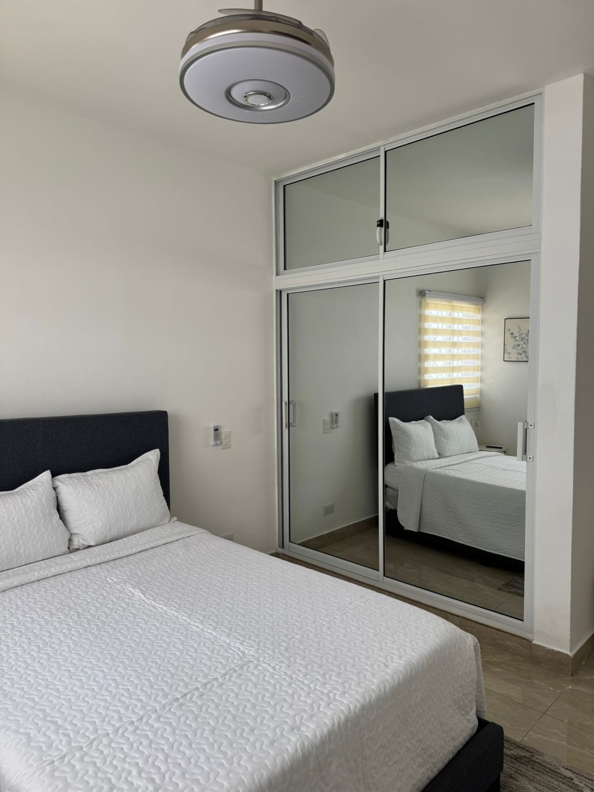 Une chambre à coucher avec un lit, une armoire avec un miroir et un luminaire au plafond.
