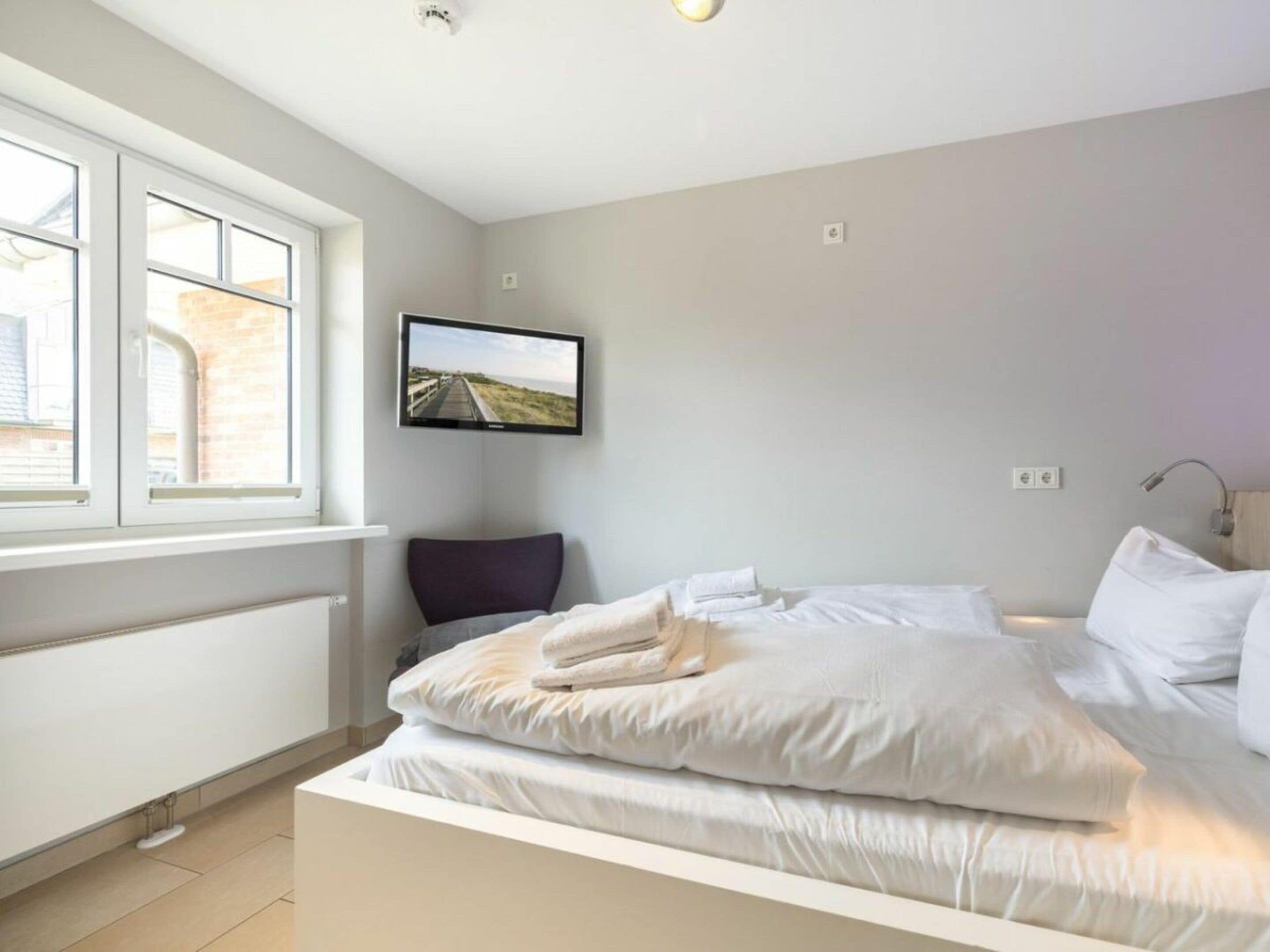 A bedroom with a bed, a television mounted on the wall, and a window providing a view outside.