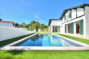 Een modern huis met een zwembad, groene luiken en een verzorgd gazon.