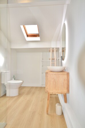 Een moderne badkamer met dakraam, toilet, wastafel en spiegel.