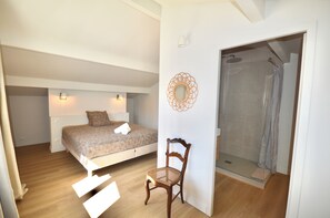 Een slaapkamer met een bed, een stoel, een douche en een spiegel aan de muur.