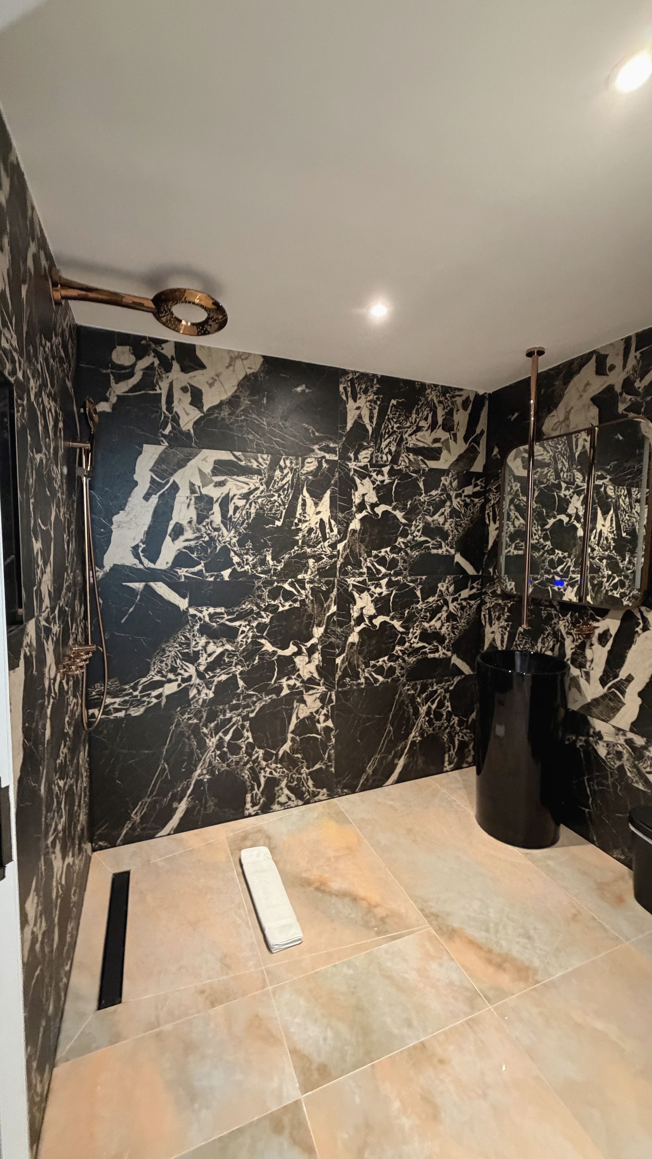 A bathroom with a marble wall, a shower area, and a towel rack.