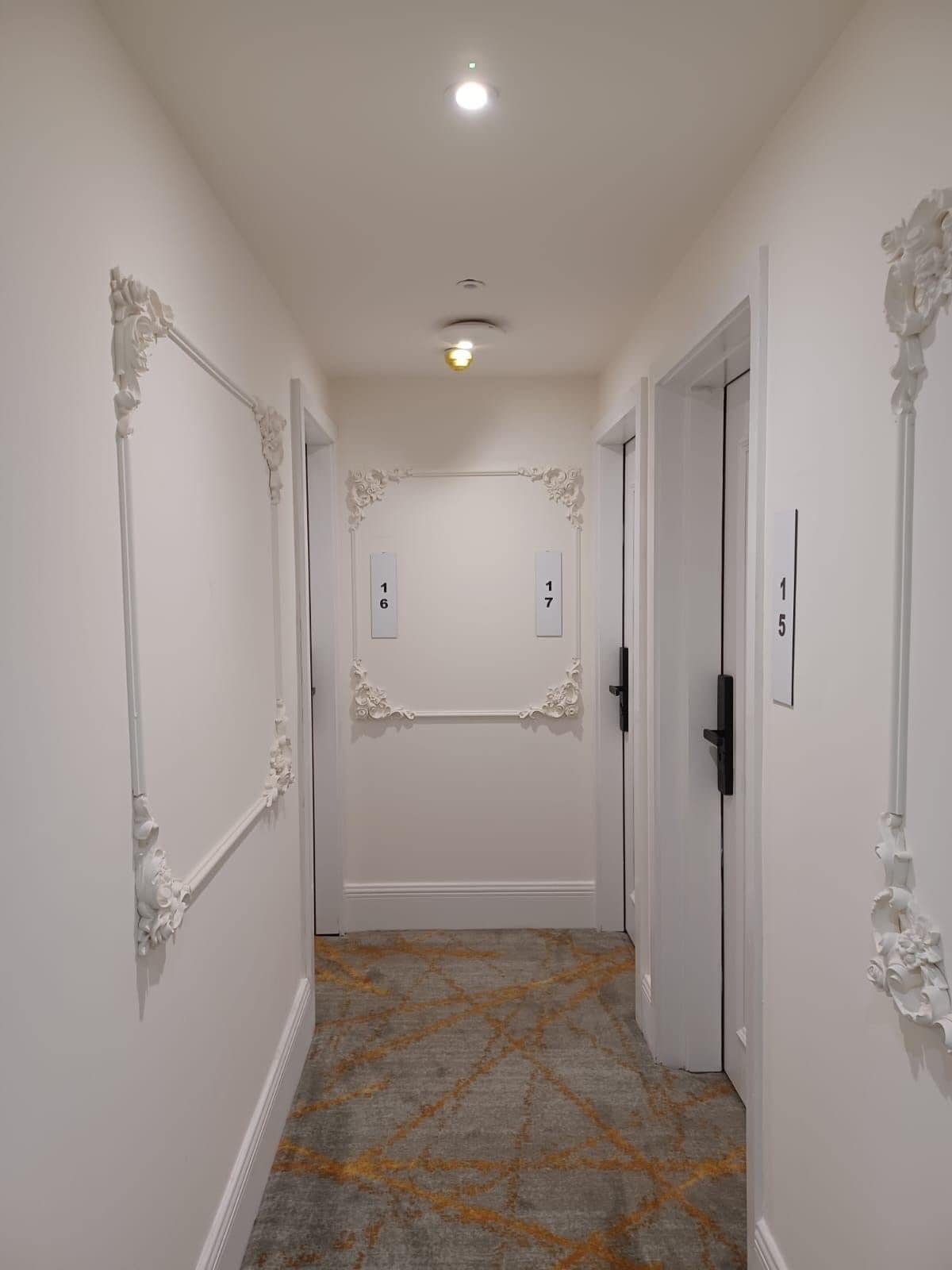 A hallway with white walls, ornate moldings, and a patterned floor.