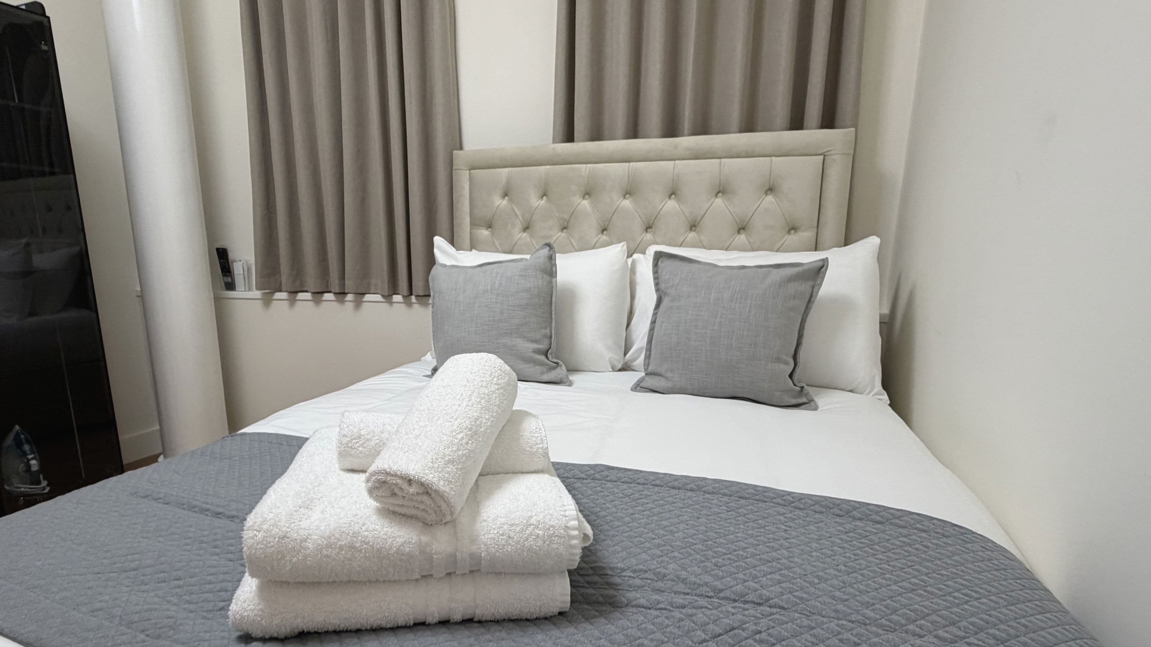 Una cama bien hecha con un edredón gris, almohadas blancas y una toalla blanca doblada encima.