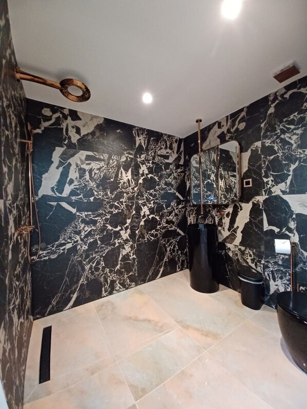 Un baño moderno con pared de mármol, un espejo grande y un lavabo negro.