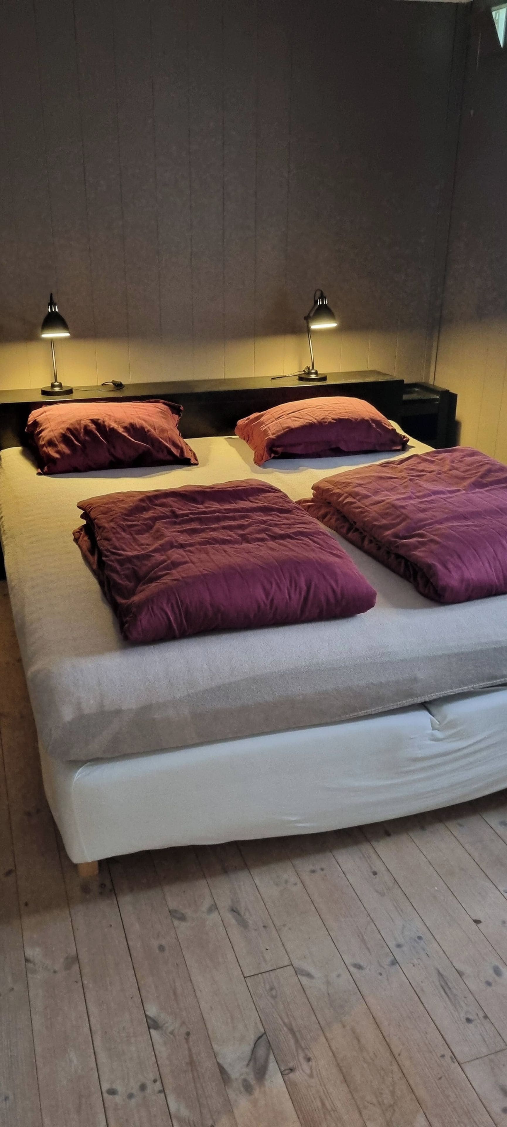A double bed with a headboard, two bedside lamps, and multiple pillows.