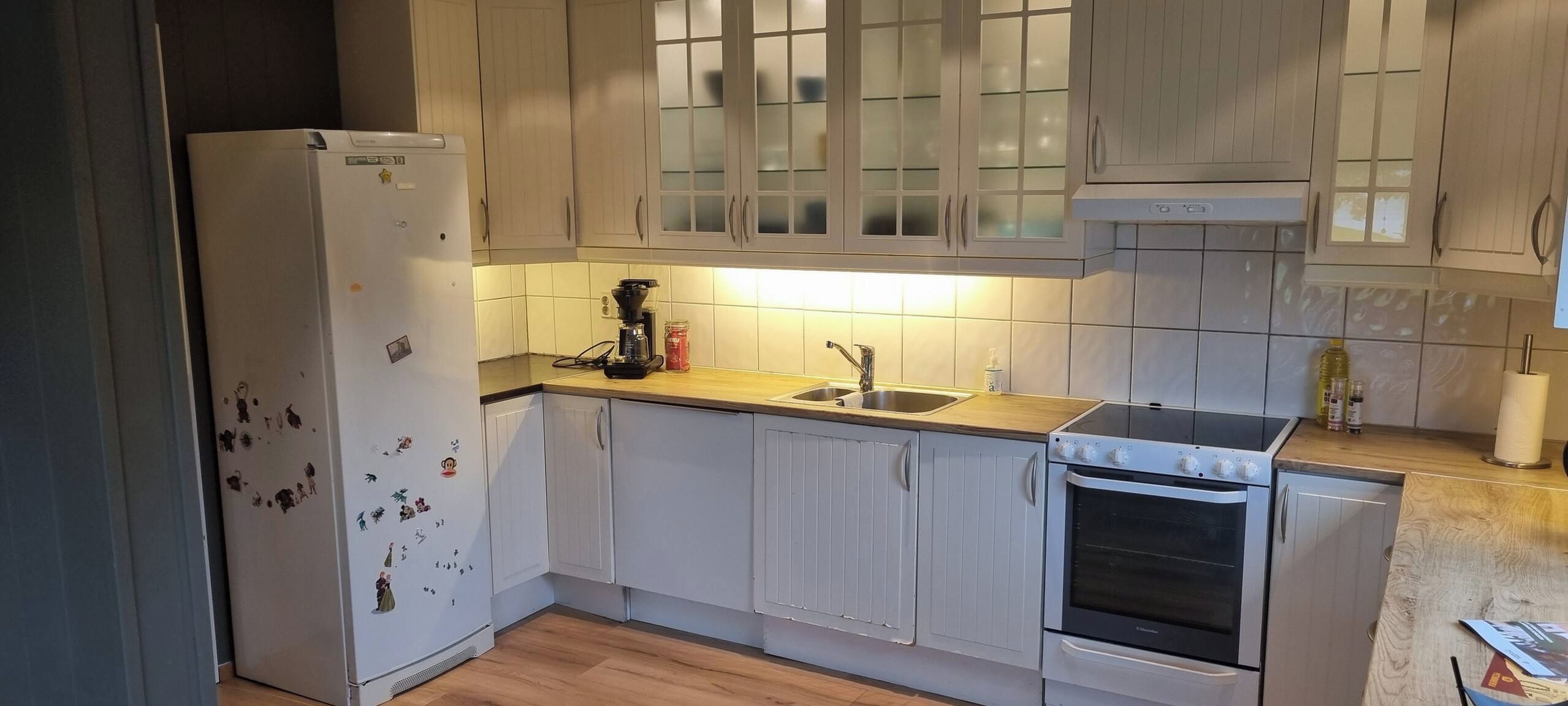 A kitchen with a refrigerator, stove, sink, and cabinets.