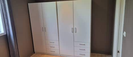 Un armario grande con varias puertas y cajones, situado en una habitación con suelo de madera y un ventanal.