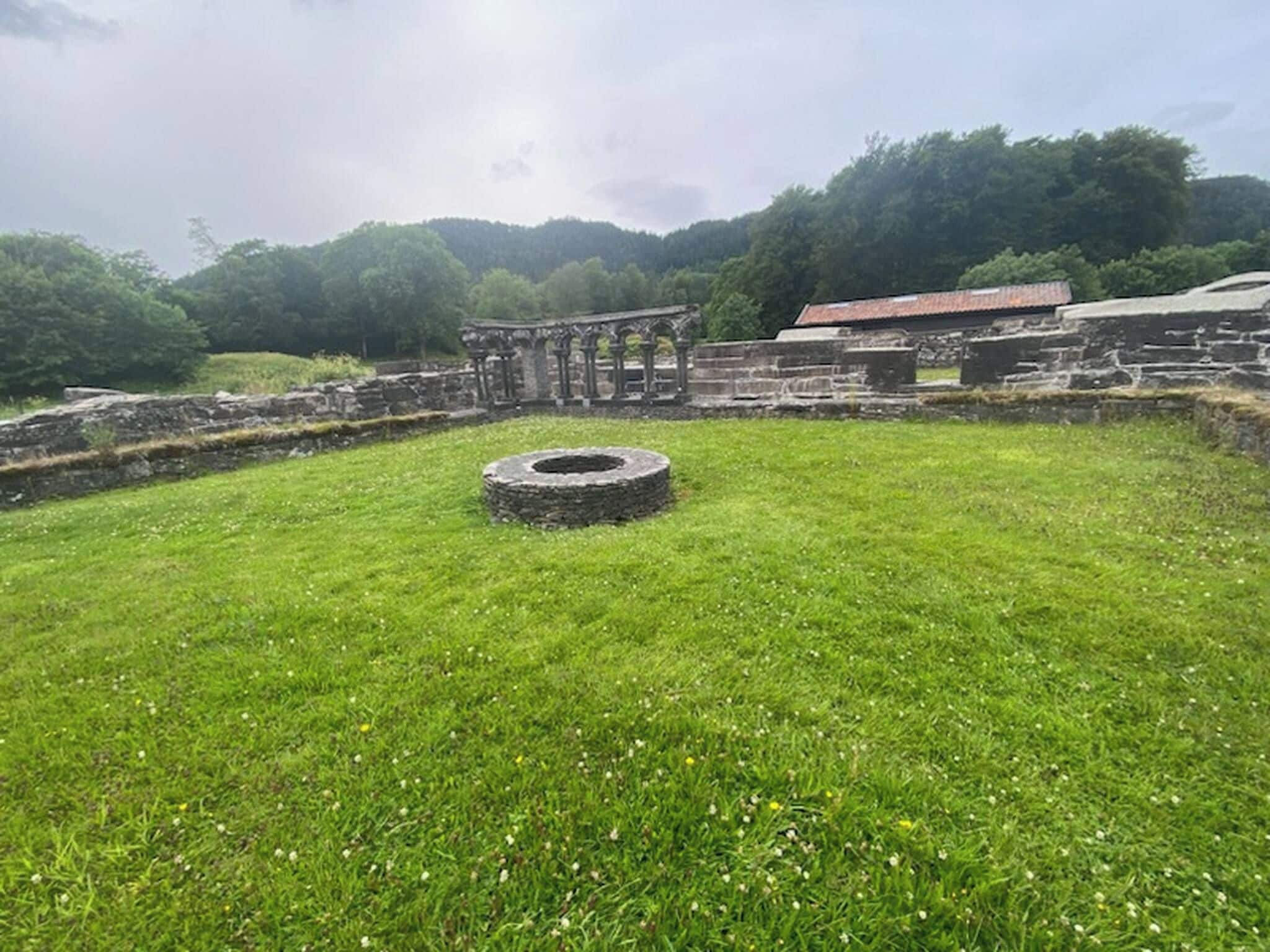 An archaeological site with stone structures and a circular stone feature in a grassy field.
