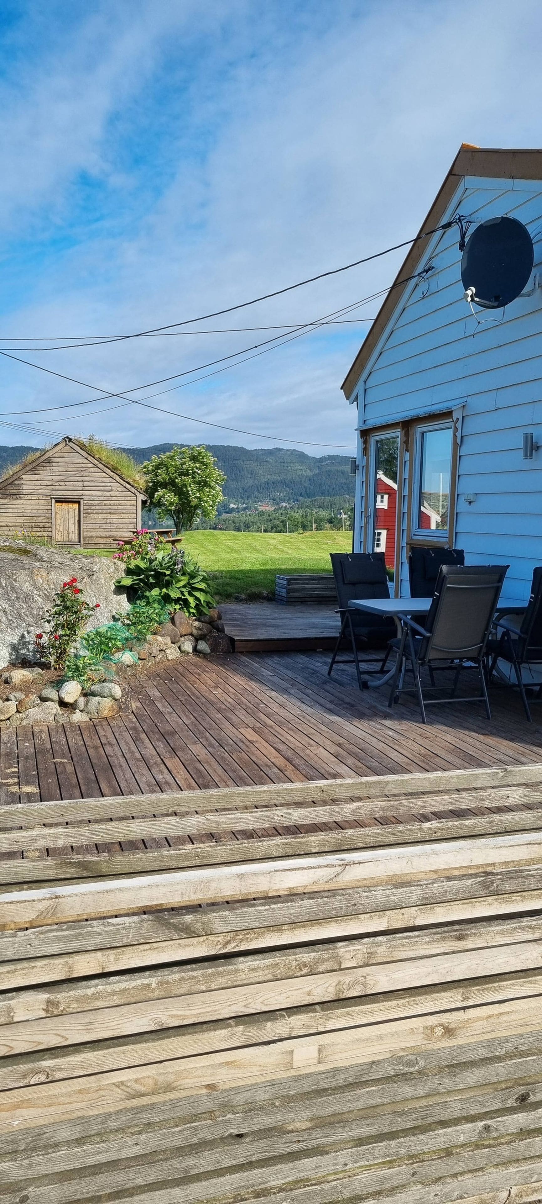A wooden deck with outdoor furniture, a house with a satellite dish, and a clear view of the surrounding landscape.