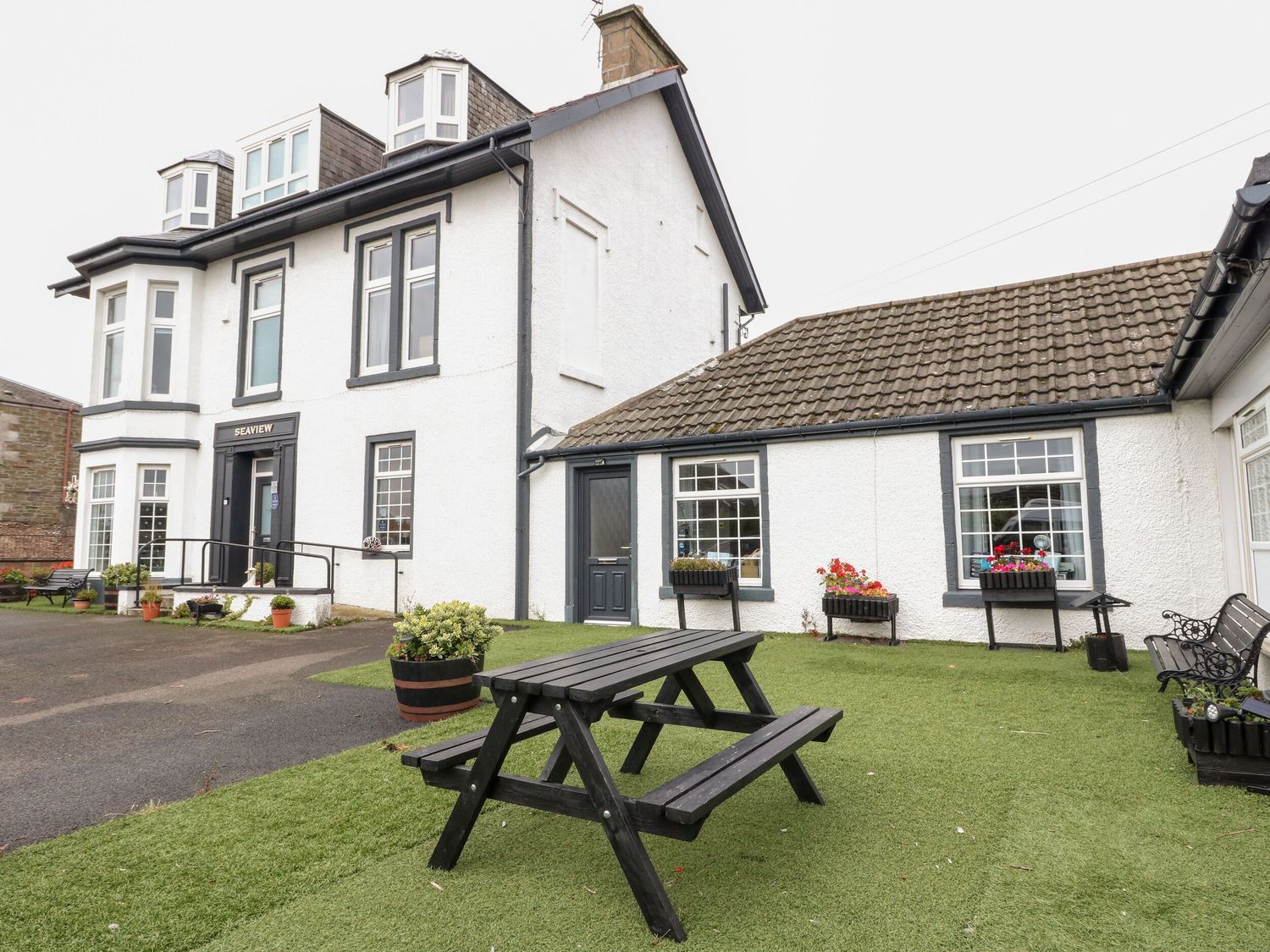 A two-story building with a black door and windows, a picnic table, and flower pots on the lawn.