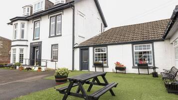A two-story building with a black door and windows, a picnic table, and flower pots on the lawn.