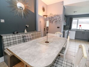 A modern kitchen with a built-in dishwasher, a dining area with a bench, and a wall-mounted clock. - Seaview House (Carnoustie)