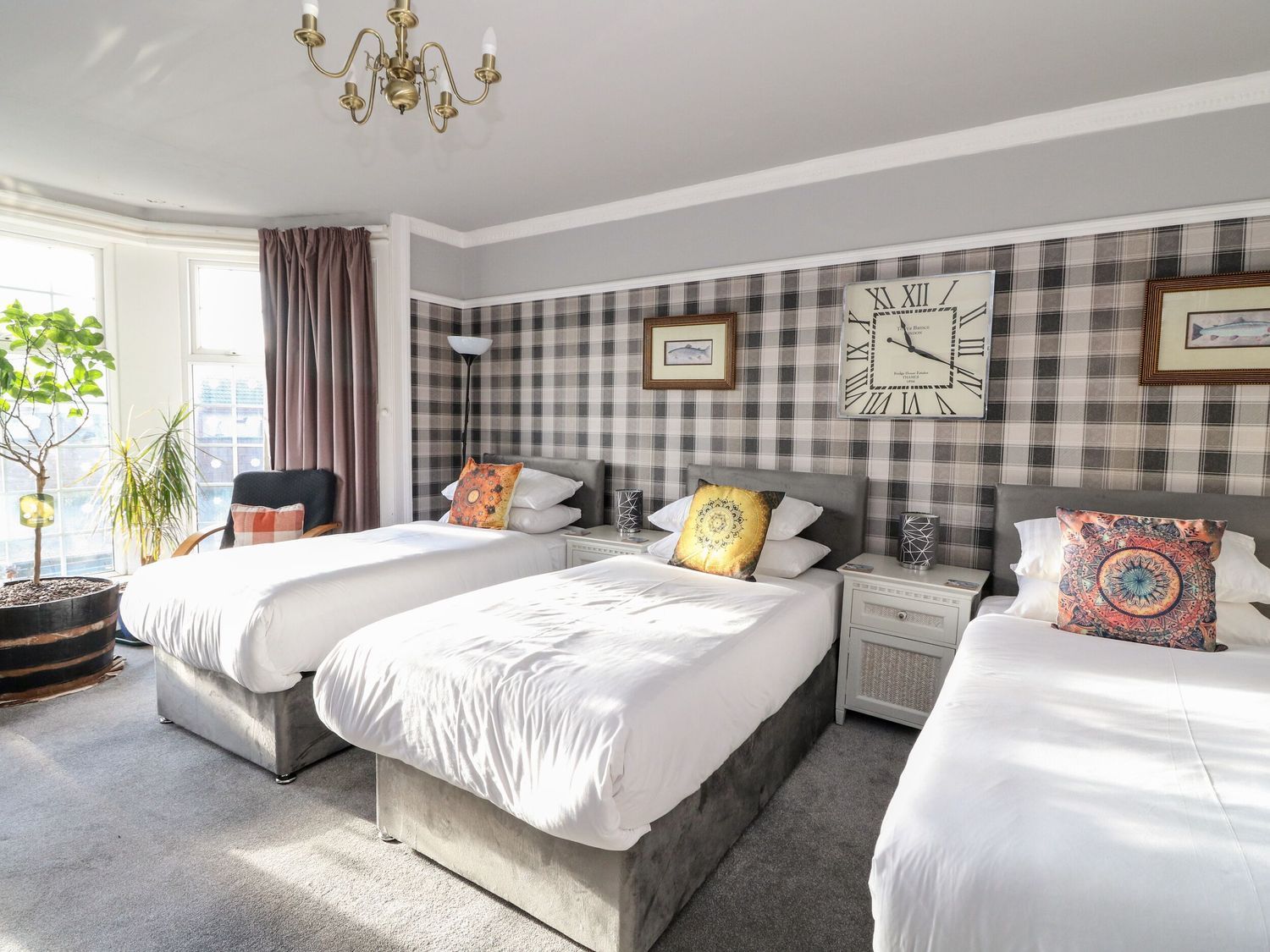 A hotel room with three beds, a large wall clock, and a window with curtains.