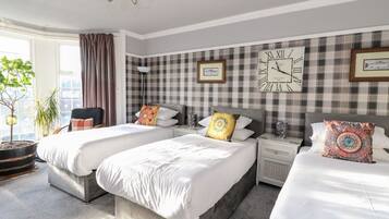 A hotel room with three beds, a large wall clock, and a window with curtains.