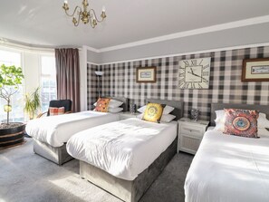 A hotel room with three beds, a large wall clock, and a window with curtains. - Seaview House (Carnoustie)
