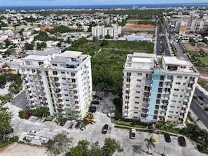 Un edificio residencial de gran altura con varios balcones, un estacionamiento y vistas del barrio circundante.
