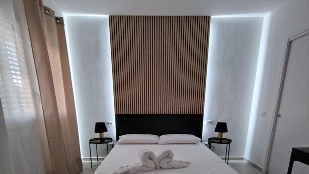 A modern hotel room with a large bed, two bedside tables, a headboard with vertical lines, and a curtain on the left. - Room '2 - Villa Fragi' with Mountain View, Wi-Fi and Air Conditioning (Cinisi)
