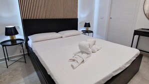 A modern hotel room with a large bed, a wooden slat wall, two bedside tables with lamps, and a door. - Room '2 - Villa Fragi' with Mountain View, Wi-Fi and Air Conditioning (Cinisi)