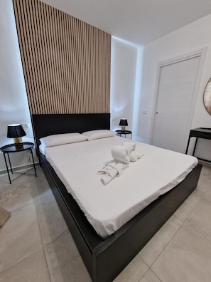 A modern hotel room with a large bed, a wooden slat wall, two bedside tables with lamps, and a door. - Room '2 - Villa Fragi' with Mountain View, Wi-Fi and Air Conditioning (Cinisi)