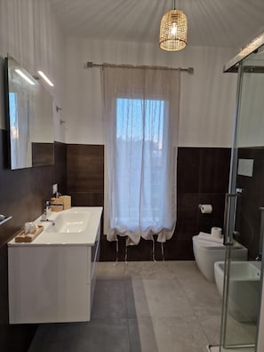 A modern bathroom with a large mirror, a white sink, a glass shower enclosure, and a hanging light fixture. - Room '3 - Villa Fragi' with Mountain View, Wi-Fi and Air Conditioning (Cinisi)