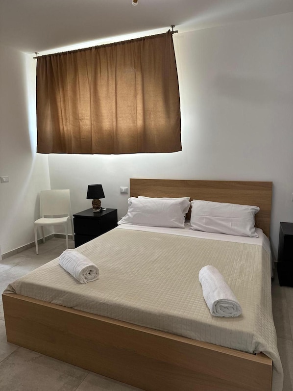 A neatly made bed with a wooden headboard, a bedside table with a lamp, and a chair. - Room '3 - Villa Fragi' with Mountain View, Wi-Fi and Air Conditioning (Cinisi)
