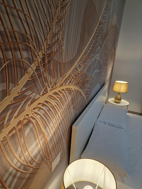 A bedroom with a large bed, a nightstand with a lamp, and a wall with a leaf-like pattern. - Room '4 - Villa Fragi' with Mountain View, Wi-Fi and Air Conditioning (Cinisi)
