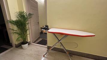 Un passadís amb una planta en test, un tauler de planxar vermell i una porta que dona a una altra habitació.