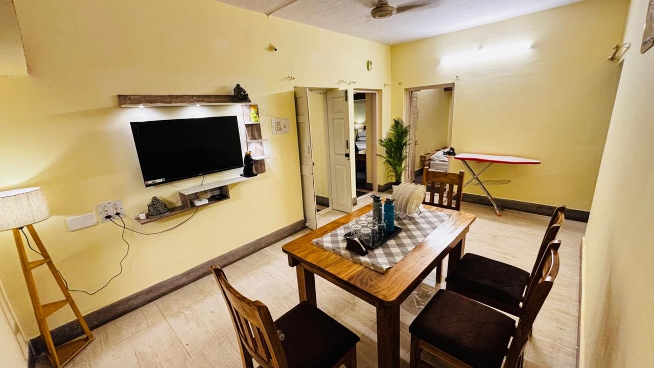 Een eetgedeelte met een tafel en stoelen, een aan de muur bevestigde televisie en een deur naar een andere kamer.