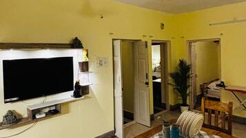 A living room with a television, a wooden dining table, and a ceiling fan.